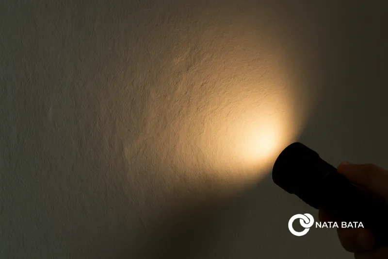 Gambar dinding rumah diperiksa menggunakan senter dari samping untuk mendeteksi permukaan bergelombang, metode pengawasan lapangan oleh tim Nata Bata