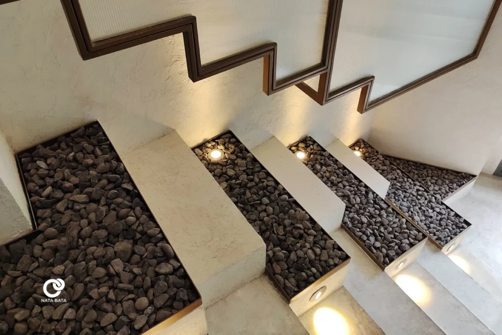 Tangga dengan elemen batu koral dan pencahayaan artistik, menghadirkan kesan alami dan elegan.