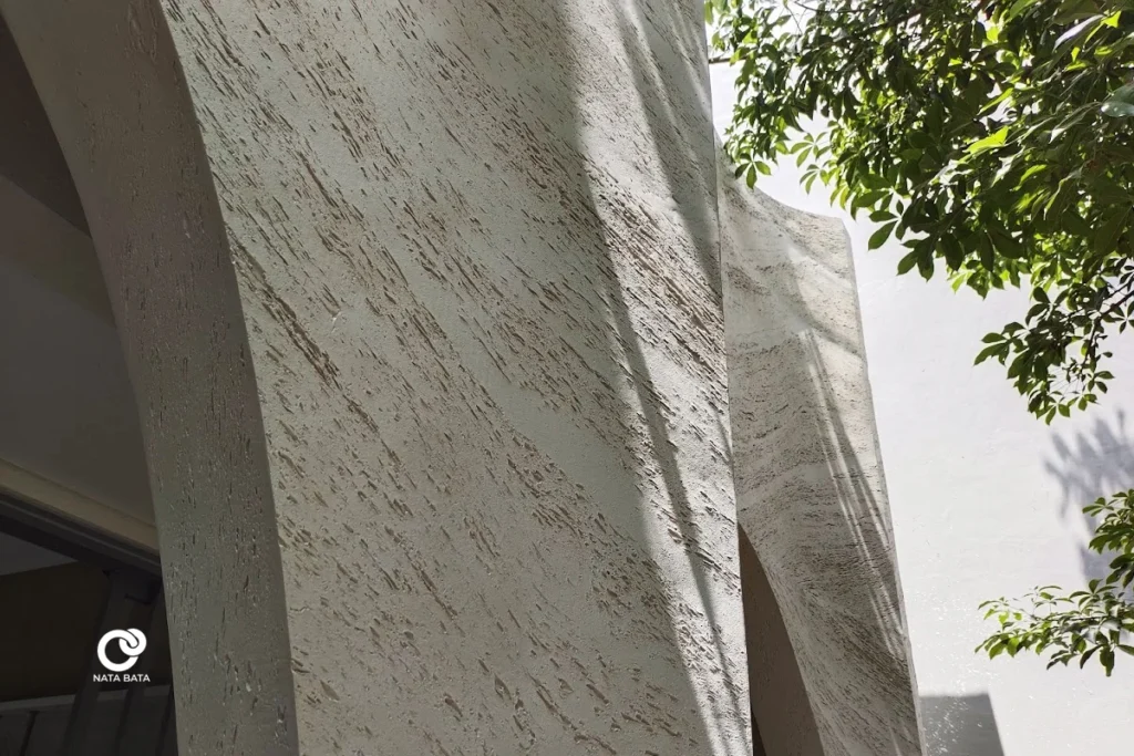 Detail tekstur travertine pada fasad melengkung, menampilkan keindahan arsitektur modern tropis karya Nata Bata.
